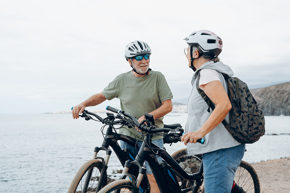 Two-older-adults-with-bicycles-talking-by-the-water
